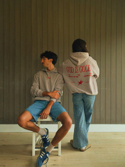 Two people wearing 'God is Good' christian hoodies in a minimalistic room.